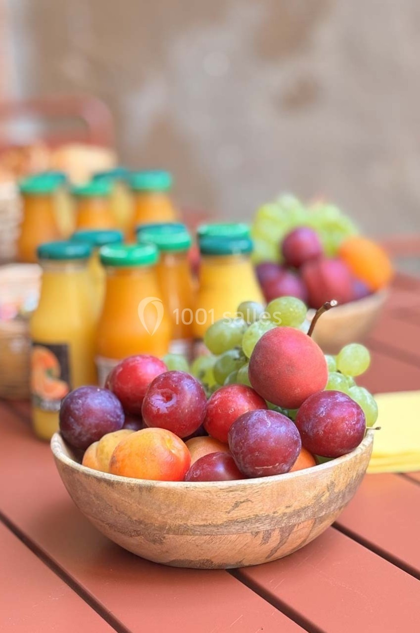 Bol de fruits variés avec prunes, raisins et abricots sur une table en bois, accompagné de bouteilles de jus.