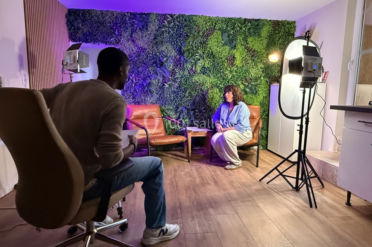 Un homme et une femme discutent dans un studio avec éclairage professionnel et mur végétal en arrière-plan.