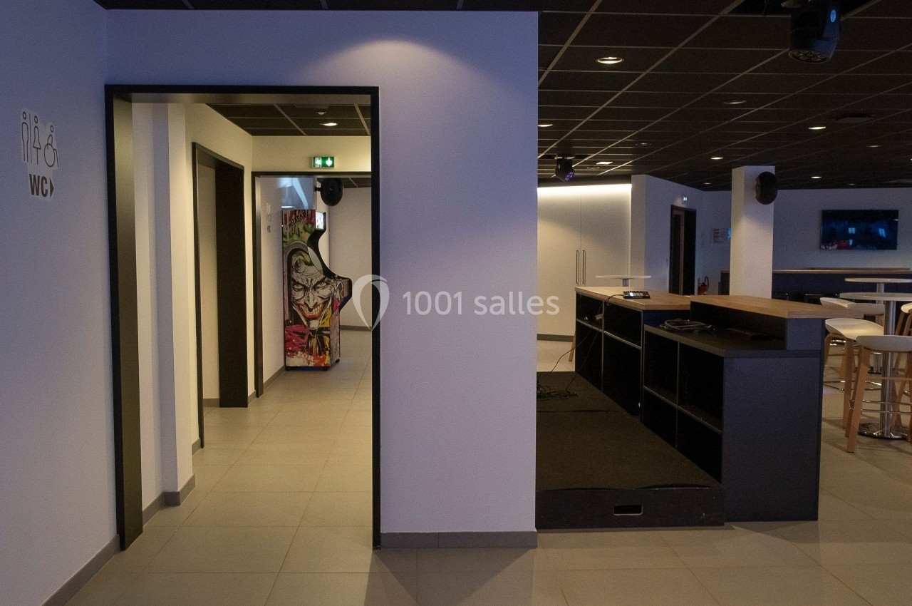 Location salle Marines (Val-d'Oise) - Stand Ing Events #2 Espace intérieur moderne avec un comptoir, des tables hautes et un couloir menant à des toilettes signalées.