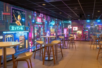 Miniature Location salle Marines (Val-d'Oise) - Stand Ing Events #18 Salle moderne avec tables hautes, éclairage tamisé, et mur décoré d'une scène urbaine nocturne avec un bistrot.