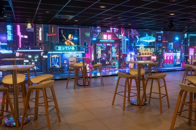 Miniature Location salle Marines (Val-d'Oise) - Stand Ing Events #19 Salle moderne avec tables hautes, éclairage tamisé, et mur décoré d'une scène urbaine nocturne avec un bistrot.