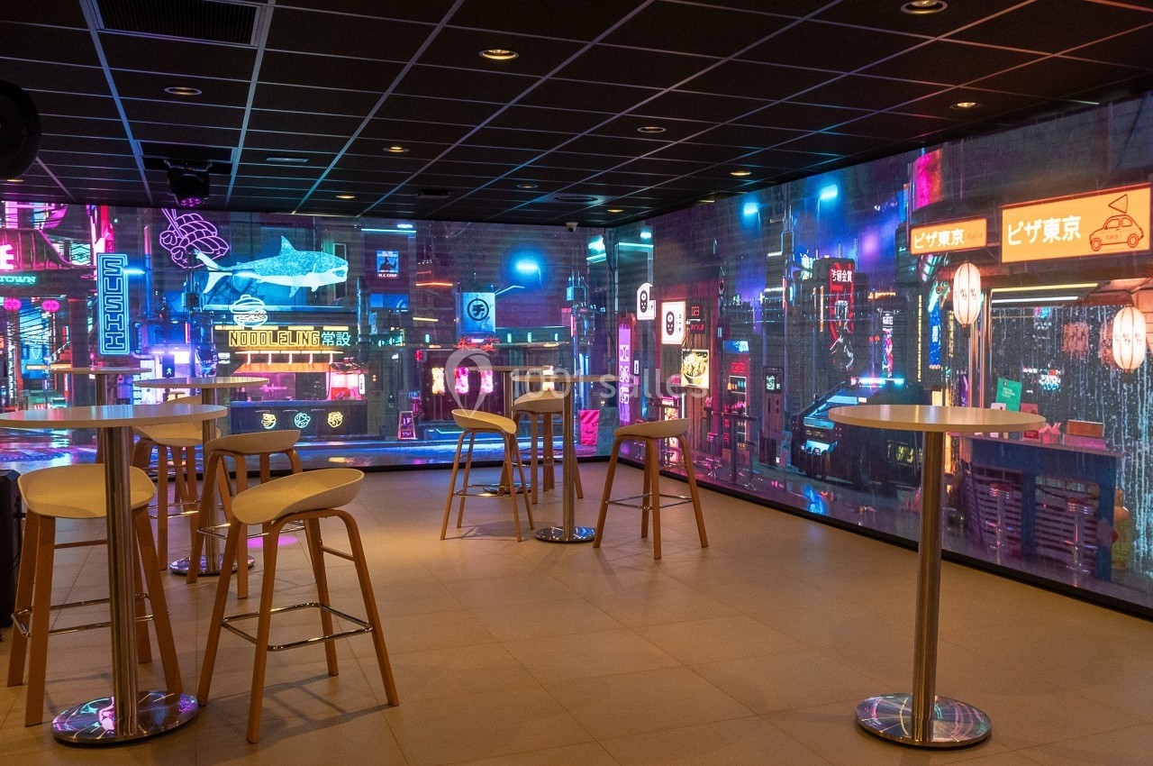 Location salle Marines (Val-d'Oise) - Stand Ing Events #22 Salle moderne avec tables hautes et décorations murales lumineuses évoquant une ambiance urbaine nocturne futuriste.
