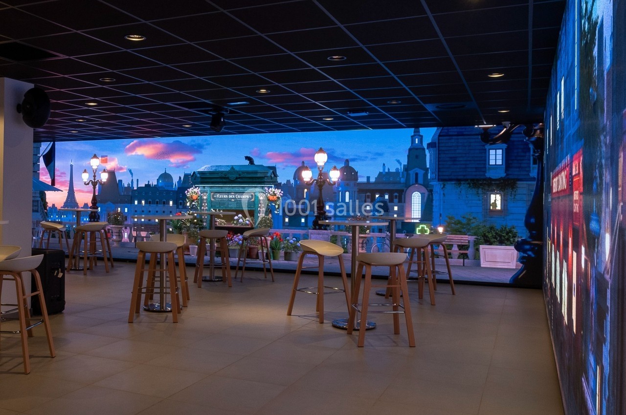 Location salle Marines (Val-d'Oise) - Stand Ing Events #23 Salle moderne avec des tables hautes, des tabourets et un écran mural affichant une vue urbaine au coucher du soleil.