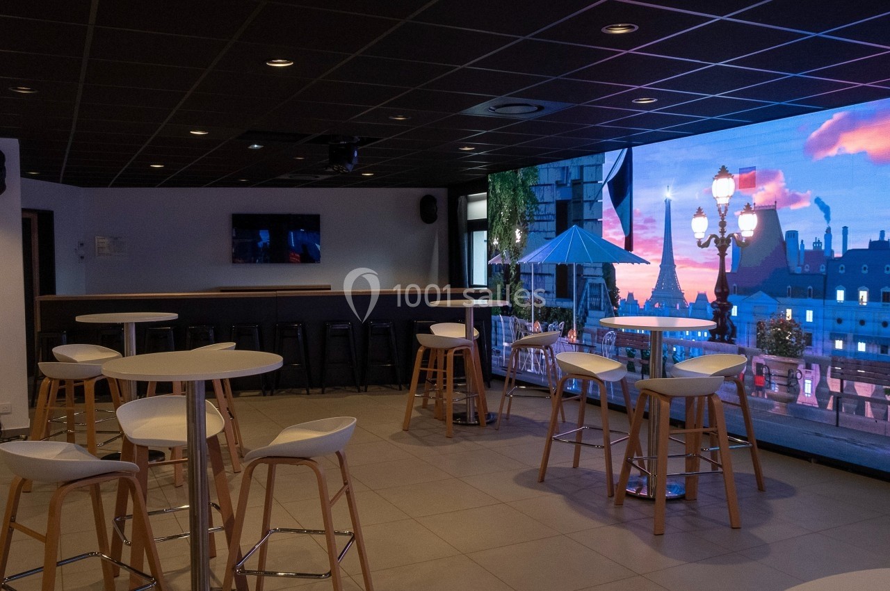 Location salle Marines (Val-d'Oise) - Stand Ing Events #25 Salle moderne avec tables hautes, tabourets et écran affichant une vue urbaine au coucher du soleil.