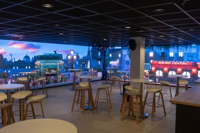 Miniature Location salle Marines (Val-d'Oise) - Stand Ing Events #29 Salle moderne avec tables hautes, éclairage tamisé, et mur décoré d'une scène urbaine nocturne avec un bistrot.