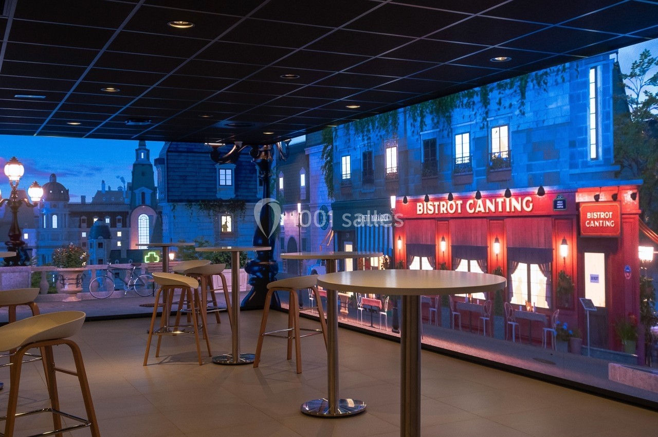 Salle moderne avec tables hautes, éclairage tamisé, et mur décoré d'une scène urbaine nocturne avec un bistrot.