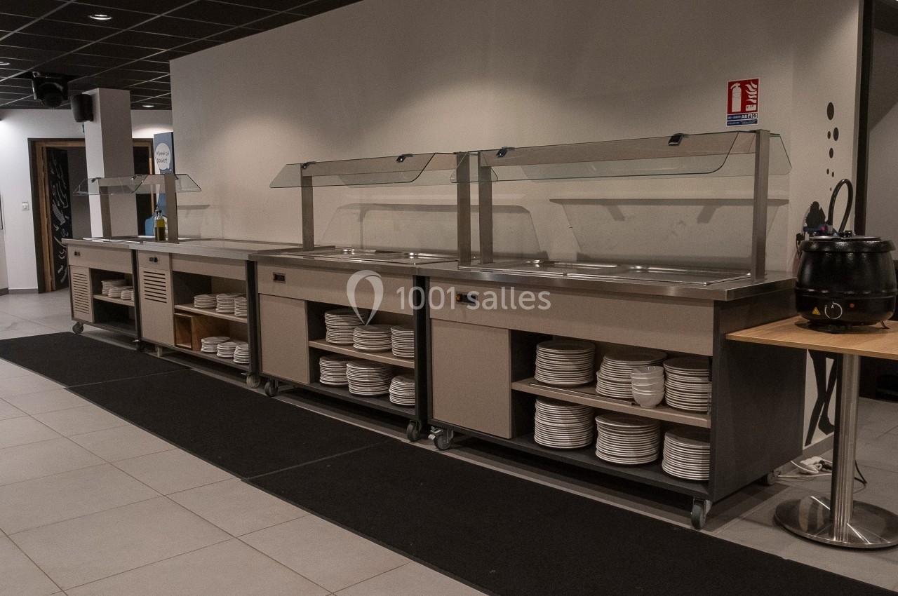 Buffet en libre-service avec comptoirs en inox, étagères contenant des assiettes et soupière à droite.