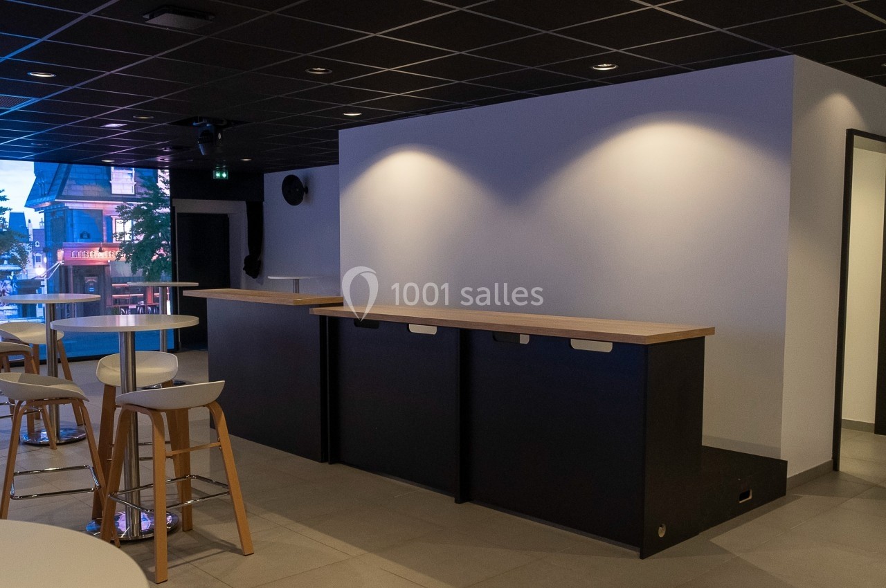 Espace intérieur moderne avec comptoir en bois, tabourets hauts et éclairage tamisé sous un plafond noir.