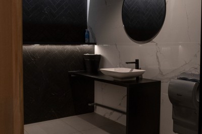 Salle de bain moderne avec lavabo, miroir rond, mur en carrelage noir et blanc, et éclairage tamisé.
