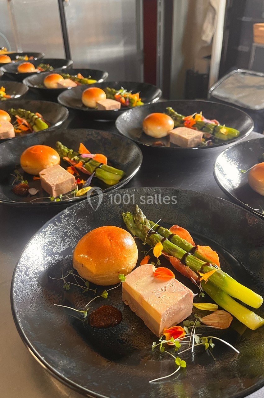 Assiettes dressées avec foie gras, asperges, pain brioché et garnitures colorées sur une table de service.