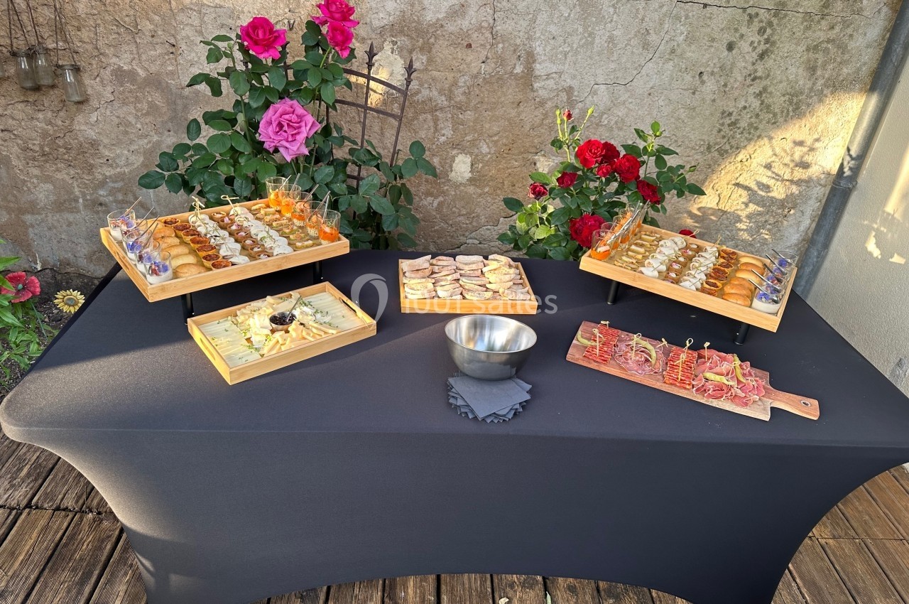 Buffet de hors-d'œuvre variés disposés sur une table noire, entourée de rosiers en fleurs dans un cadre extérieur.