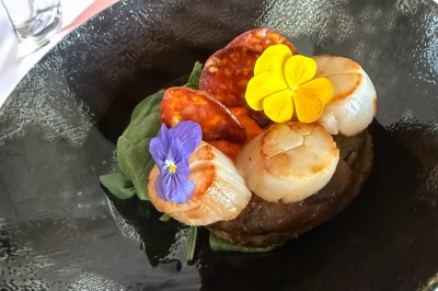 Salle décorée pour les fêtes avec guirlandes lumineuses, table rouge ornée de bougies et mini sapins, scène en arrière-plan.