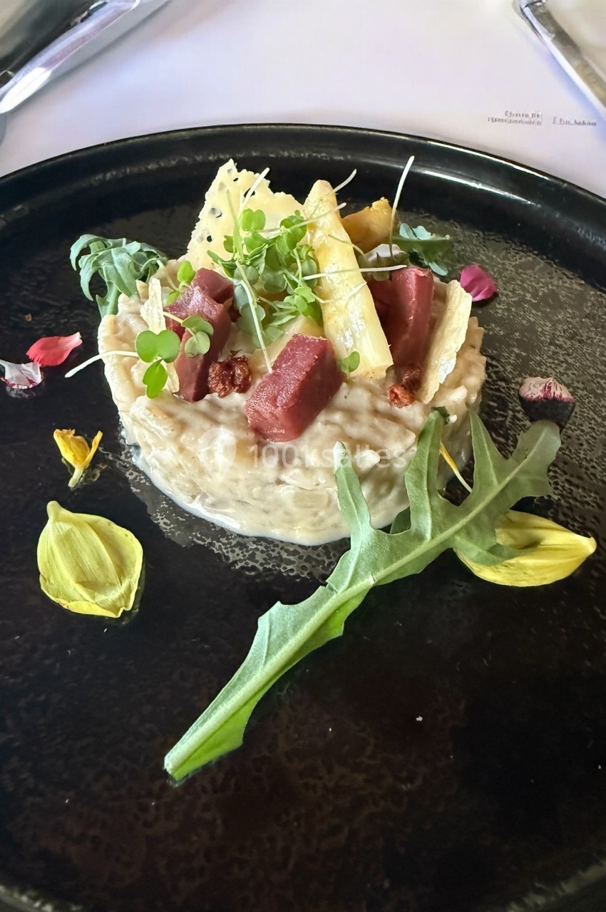 Assiette de risotto crémeux garni de morceaux de viande, asperges, roquette et pétales de fleurs comestibles.