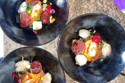 Salle décorée pour les fêtes avec guirlandes lumineuses, table rouge ornée de bougies et mini sapins, scène en arrière-plan.