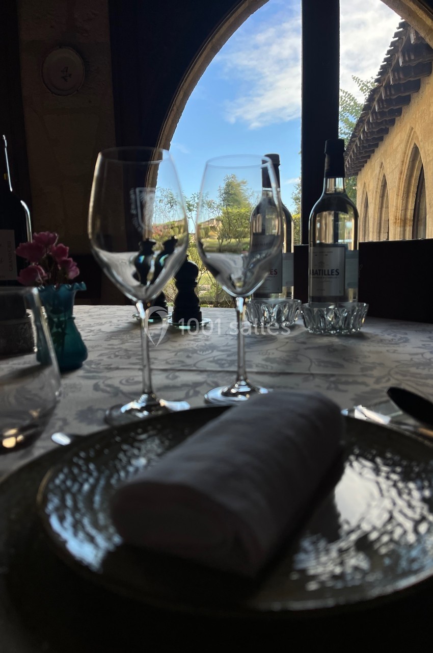 Table élégamment dressée avec vue sur un jardin à travers une grande arche, verres et bouteilles en premier plan.