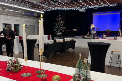 Salle décorée pour les fêtes avec guirlandes lumineuses, table rouge ornée de bougies et mini sapins, scène en arrière-plan.