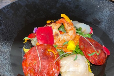 Salle décorée pour les fêtes avec guirlandes lumineuses, table rouge ornée de bougies et mini sapins, scène en arrière-plan.