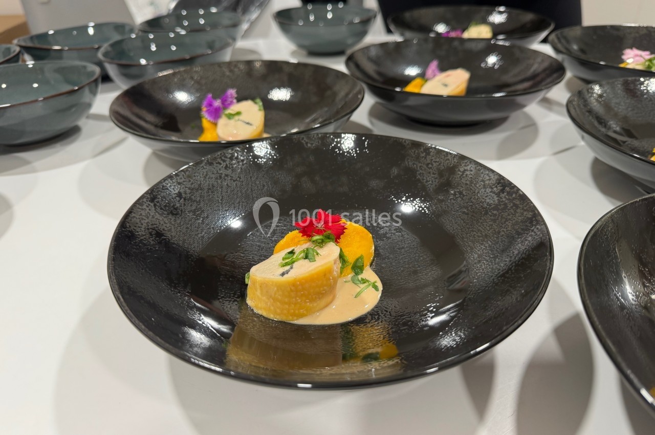 Assiette noire contenant une présentation soignée de légumes, sauce crémeuse et décoration florale comestible.