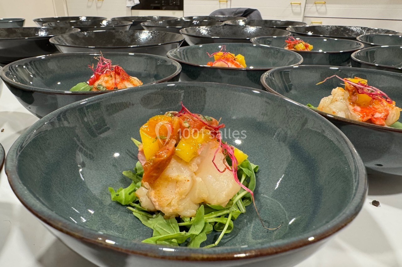 Assiette de salade avec langoustine, mangue et micro-pousses, servie dans un bol en céramique sur une table.