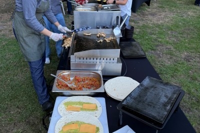 Préparation de wraps avec des ingrédients comme fromage, guacamole et poulet grillé sur une plancha en extérieur.