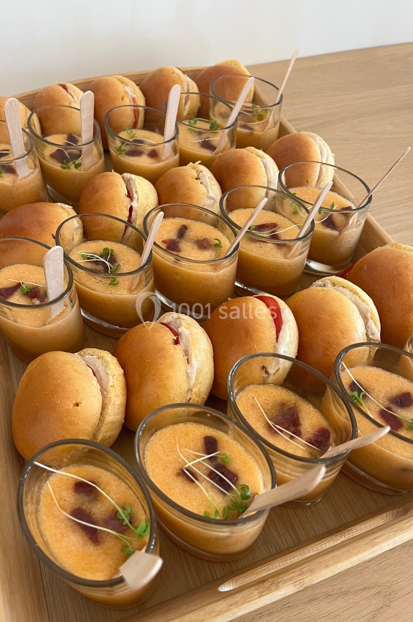 Plateau de mini-burgers et verrines de soupe garnies de fines herbes, présenté sur une table en bois.