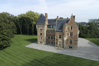 Vue aérienne d'un château en briques rouges entouré de pelouses bien entretenues et d'arbres.
