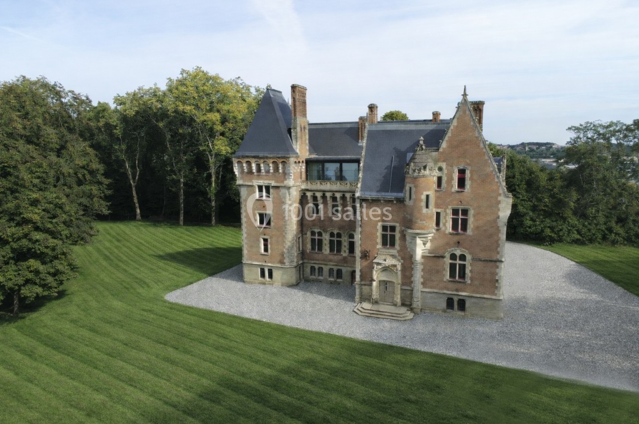 Vue aérienne d'un château en briques rouges entouré de pelouses bien entretenues et d'arbres.