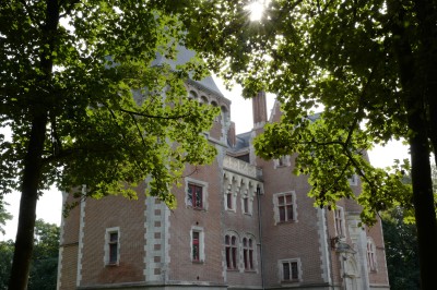 Vue aérienne d'un château en briques rouges entouré de pelouses bien entretenues et d'arbres.