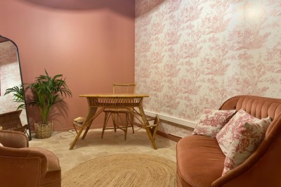 Fauteuil bleu et table basse dans un salon au style vintage avec papier peint fleuri et armoire en bois.