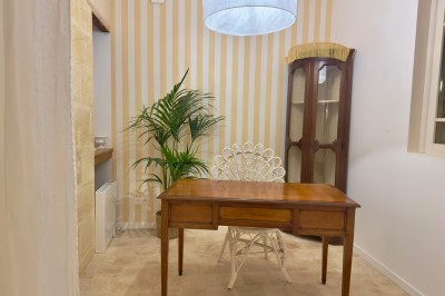 Fauteuil bleu et table basse dans un salon au style vintage avec papier peint fleuri et armoire en bois.