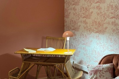 Fauteuil bleu et table basse dans un salon au style vintage avec papier peint fleuri et armoire en bois.
