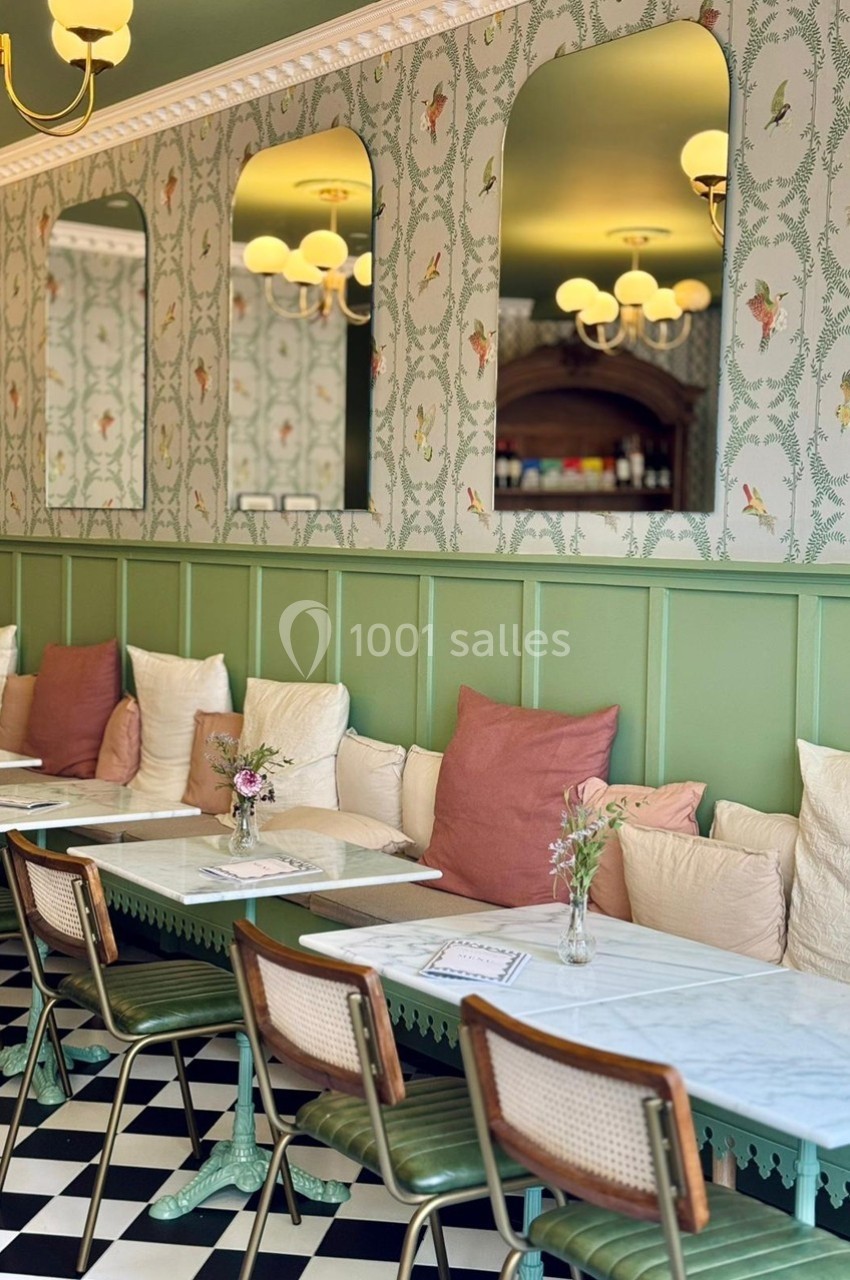Salle de restaurant lumineuse avec murs verts, banquette garnie de coussins et tables alignées sur un sol en damier.