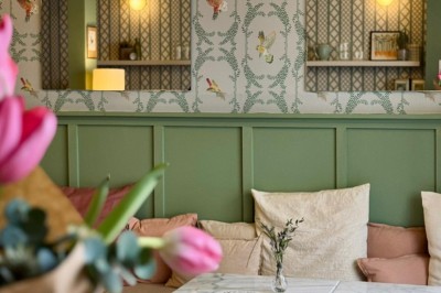 Fauteuil bleu et table basse dans un salon au style vintage avec papier peint fleuri et armoire en bois.