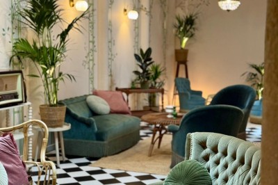 Fauteuil bleu et table basse dans un salon au style vintage avec papier peint fleuri et armoire en bois.