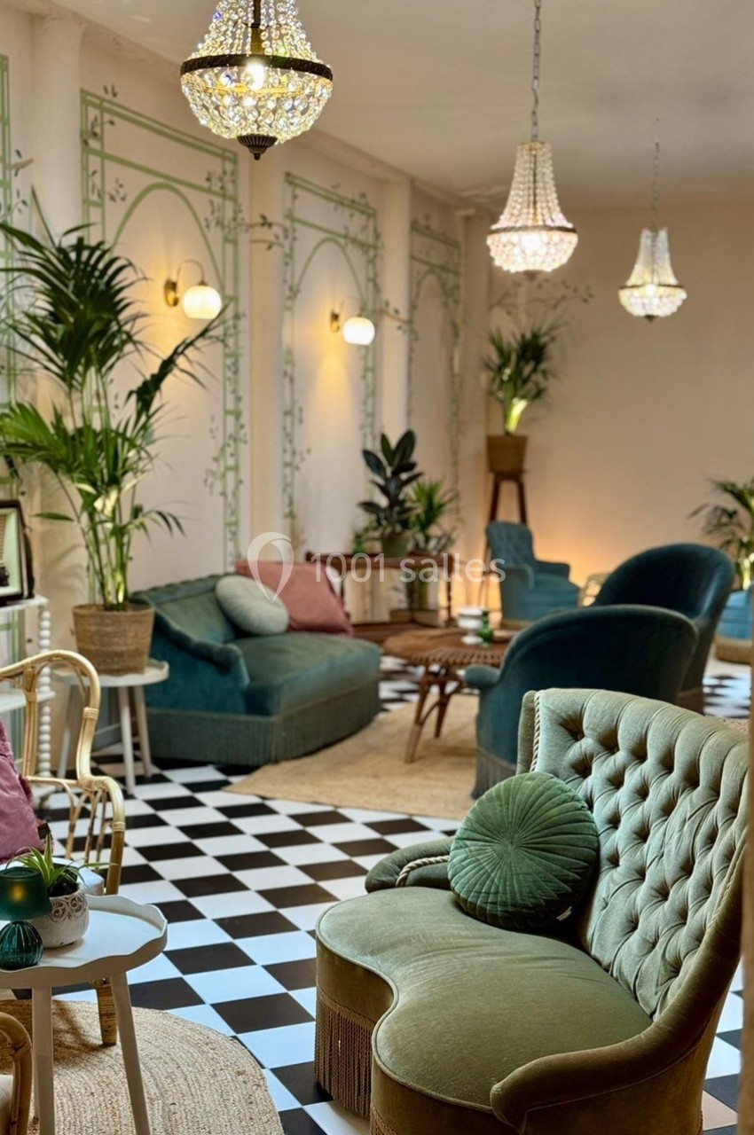 Salon élégant avec fauteuils verts, plantes, lustres en cristal et sol en damier noir et blanc.