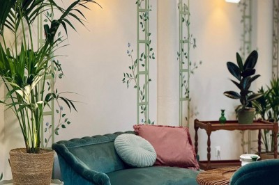 Fauteuil bleu et table basse dans un salon au style vintage avec papier peint fleuri et armoire en bois.