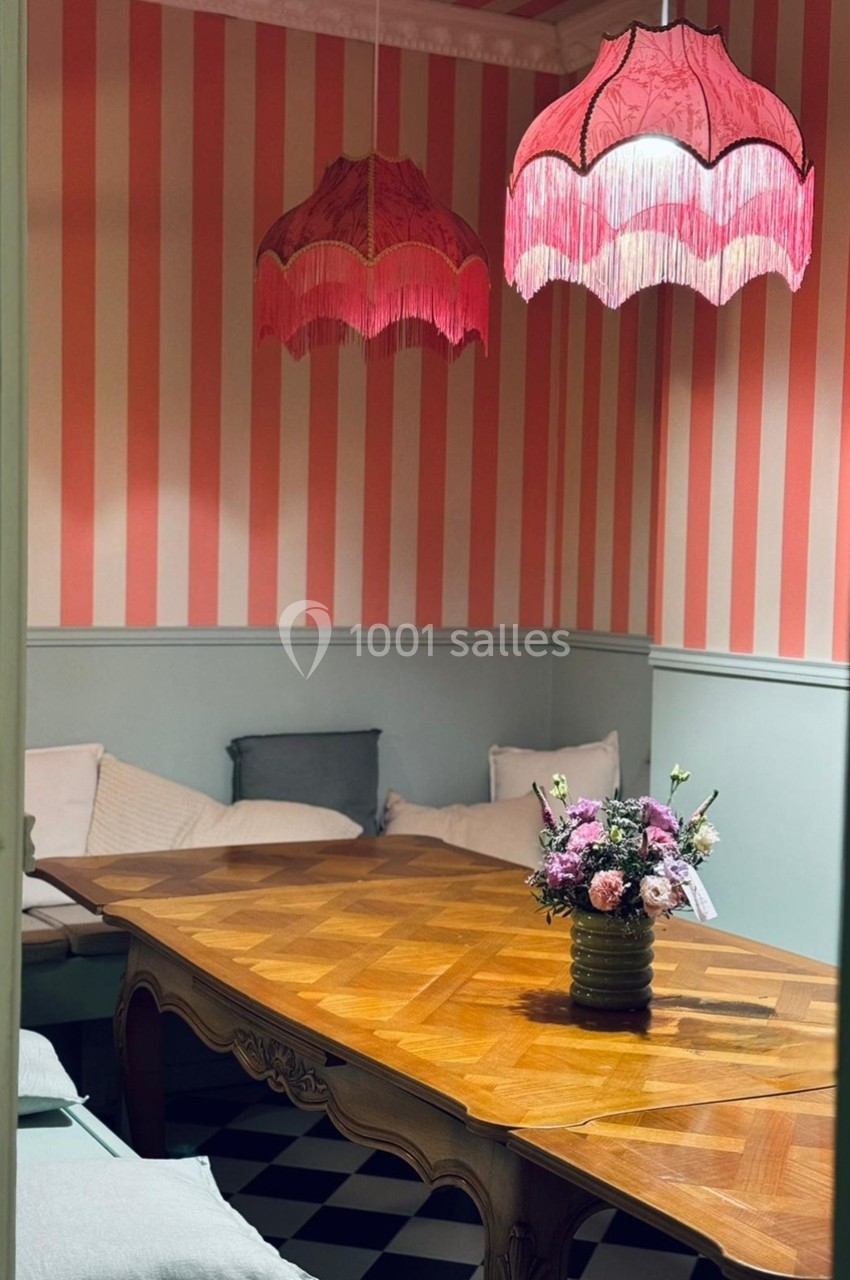 Salle à manger avec table en bois, bouquet de fleurs, banquettes et lampes suspendues roses à franges.