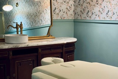 Fauteuil bleu et table basse dans un salon au style vintage avec papier peint fleuri et armoire en bois.