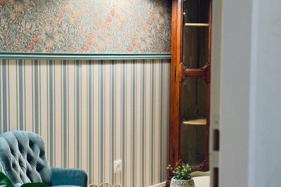 Fauteuil bleu et table basse dans un salon au style vintage avec papier peint fleuri et armoire en bois.