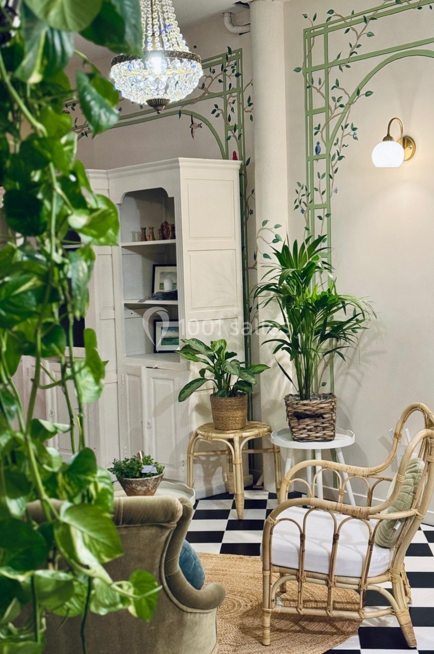 Espace intérieur lumineux avec des plantes, des meubles en rotin, un sol en damier et une armoire blanche.