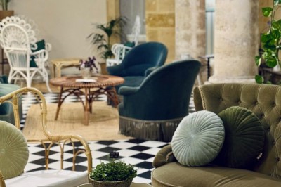 Fauteuil bleu et table basse dans un salon au style vintage avec papier peint fleuri et armoire en bois.