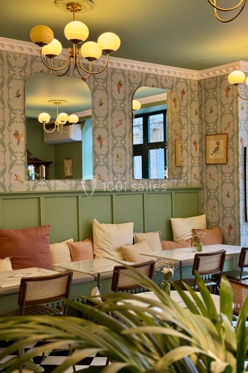Salle de restaurant lumineuse avec banquette, coussins colorés, miroirs et décoration murale à motifs floraux.