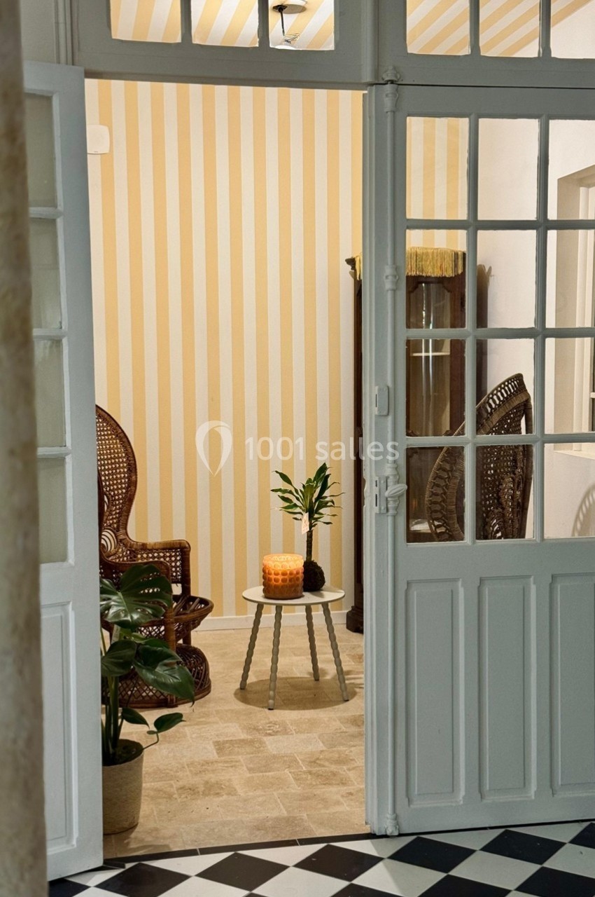 Vue d'un salon lumineux avec fauteuils en rotin, table basse décorée d'une plante et bougie, sol en pierre beige.
