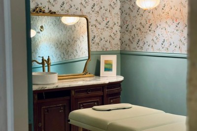 Fauteuil bleu et table basse dans un salon au style vintage avec papier peint fleuri et armoire en bois.