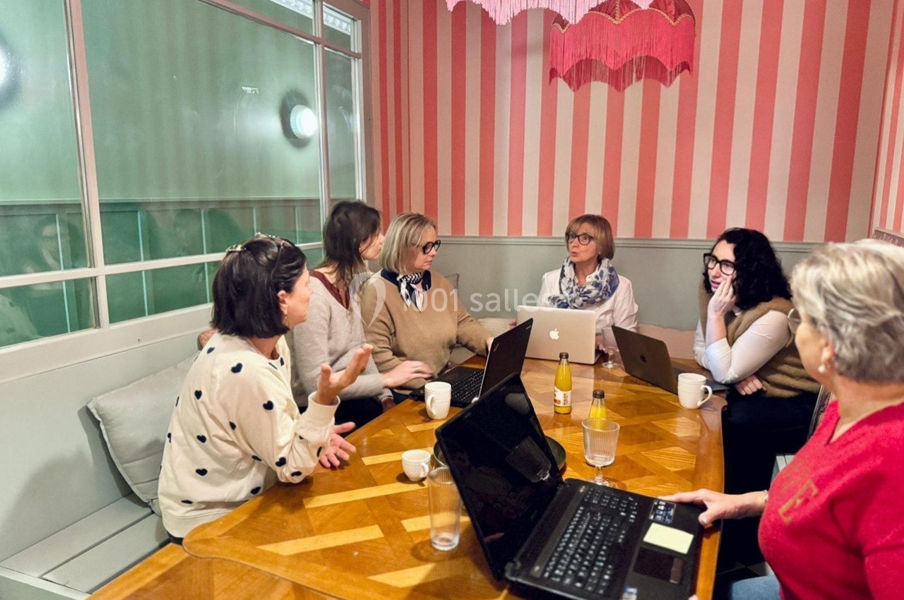 Six femmes discutent autour d'une table en bois, avec des ordinateurs portables et des boissons, dans une salle aux murs…
