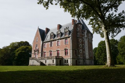 Vue aérienne d'un château en briques rouges entouré d'une pelouse bien entretenue et d'arbres.