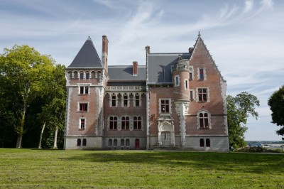 Vue aérienne d'un château en briques rouges entouré d'une pelouse bien entretenue et d'arbres.