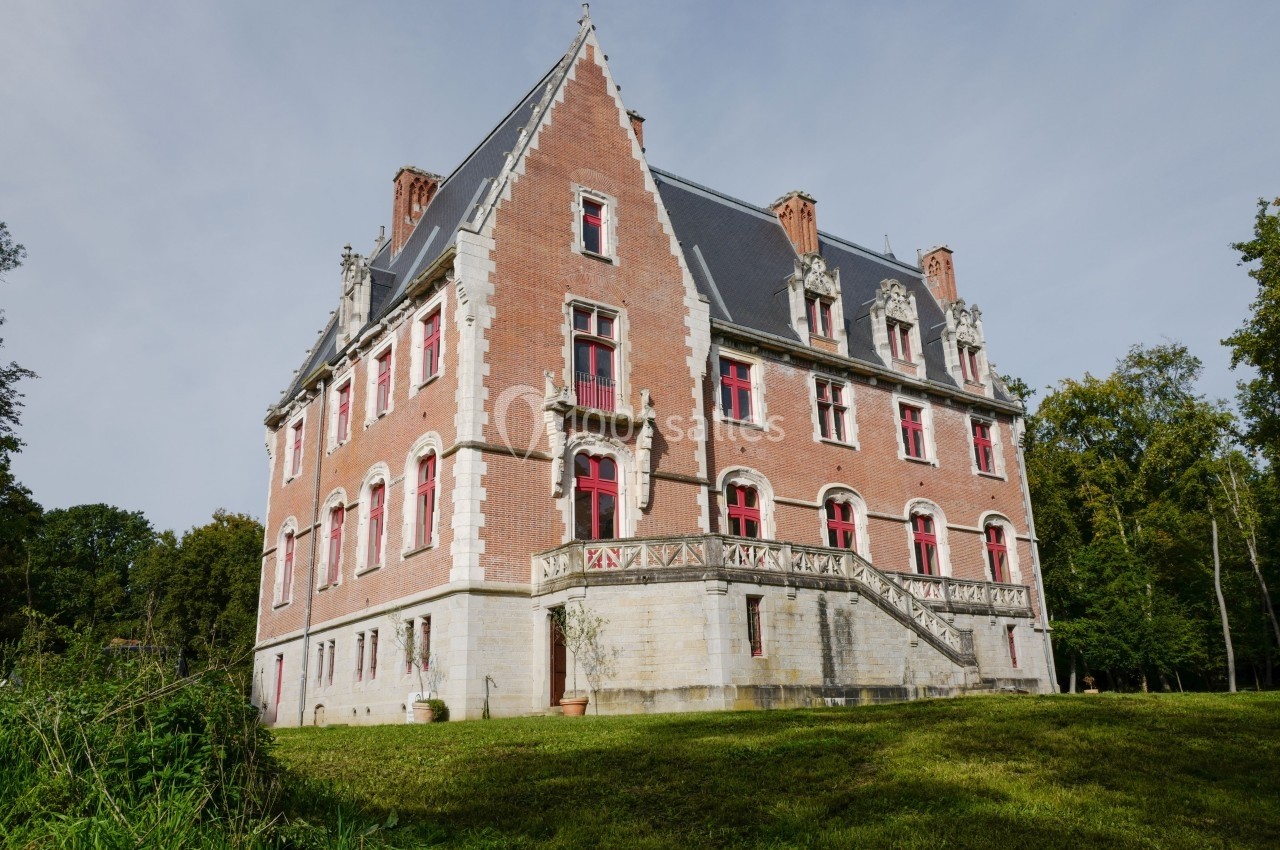 Façade d'un château en briques rouges avec des fenêtres à encadrement blanc, entouré de verdure.