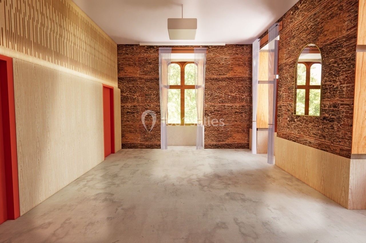 Salle lumineuse avec murs en pierre et bois, fenêtres cintrées, sol en béton et portes rouges.