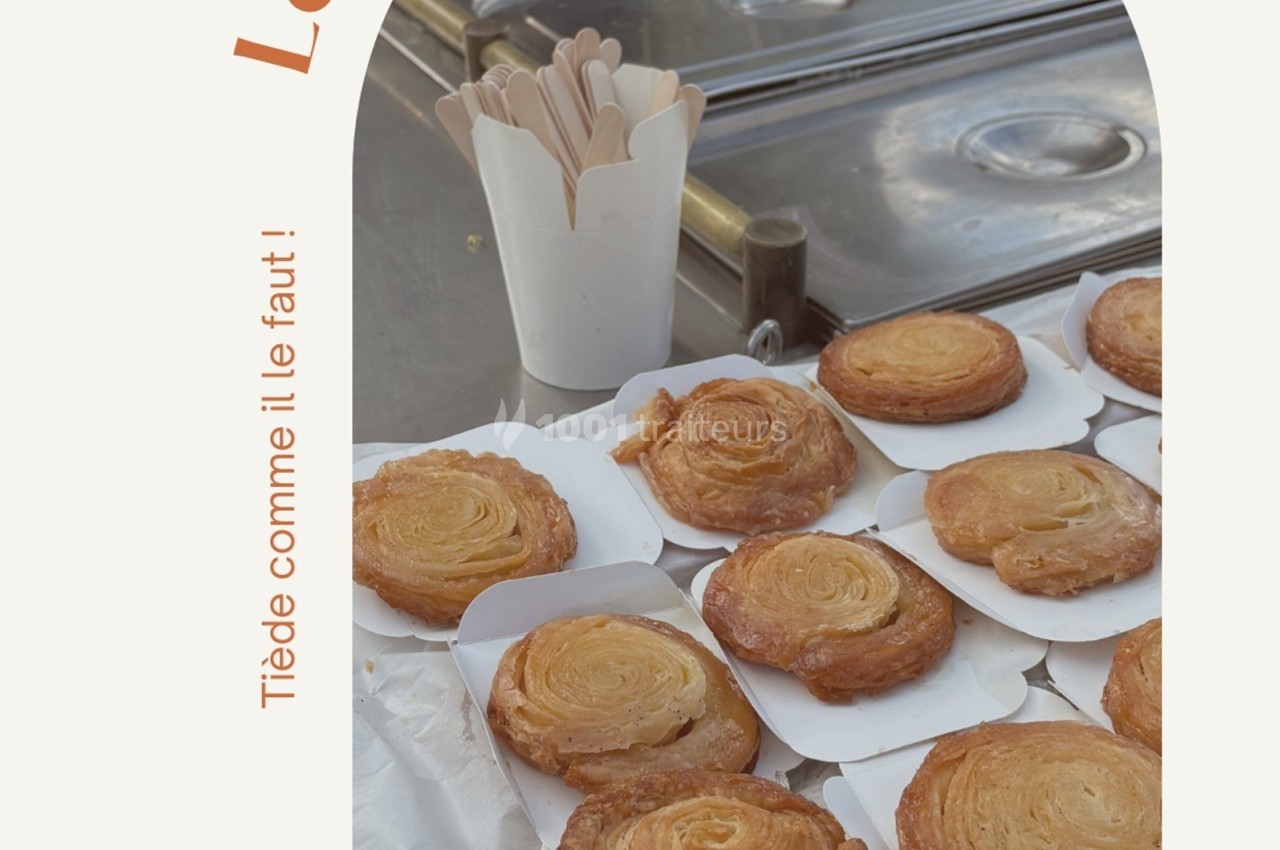 Des pâtisseries feuilletées dorées disposées sur des assiettes en carton, avec des cuillères en bois dans un pot.